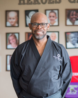Man in black martial arts uniform smiling in front of photo wall.