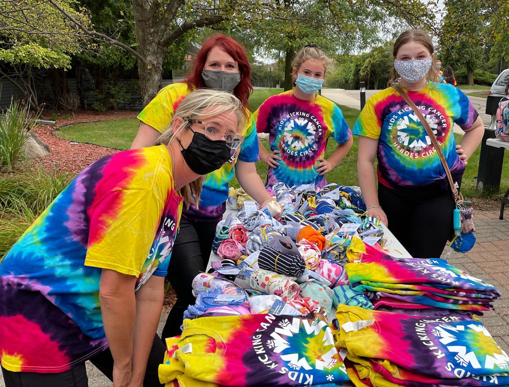 VE1Z3830 (3) Group of women in tie-dye shirts and masks at outdoor event table.