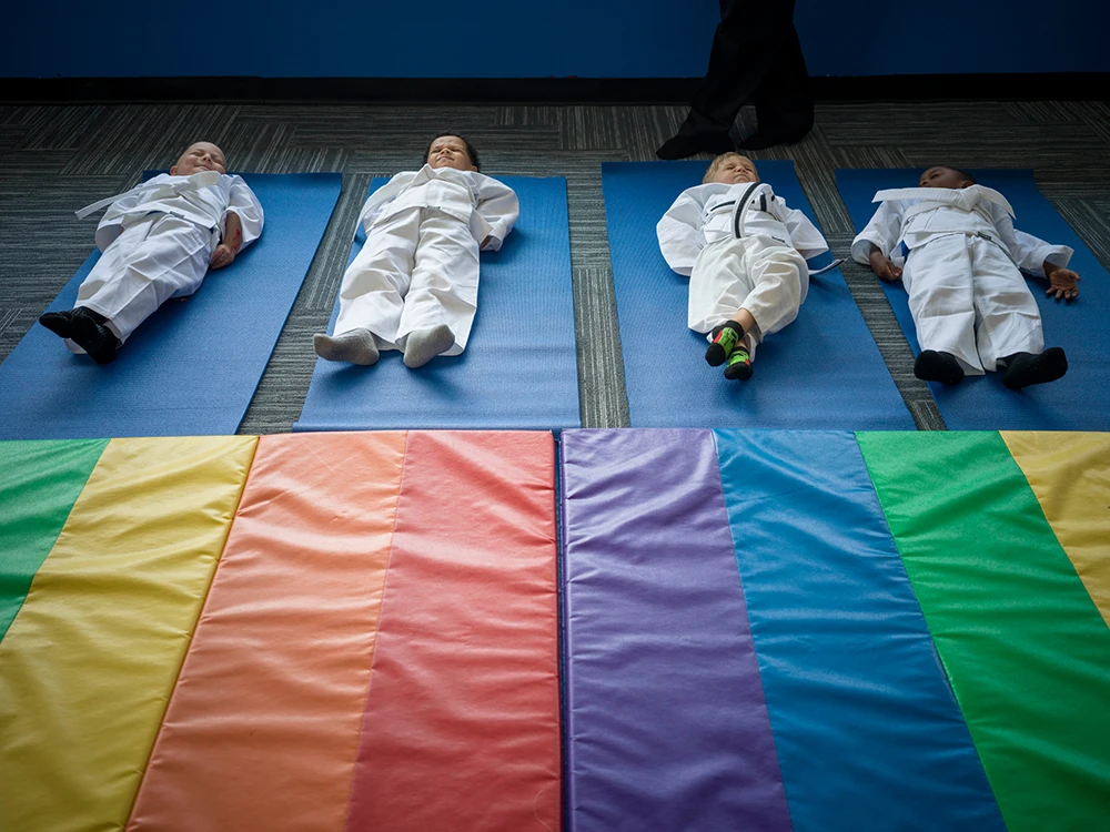 Four children in martial arts uniforms lying on blue mats.