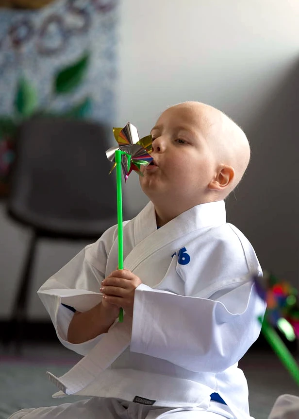 Child in martial arts uniform blowing on a colorful pinwheel.