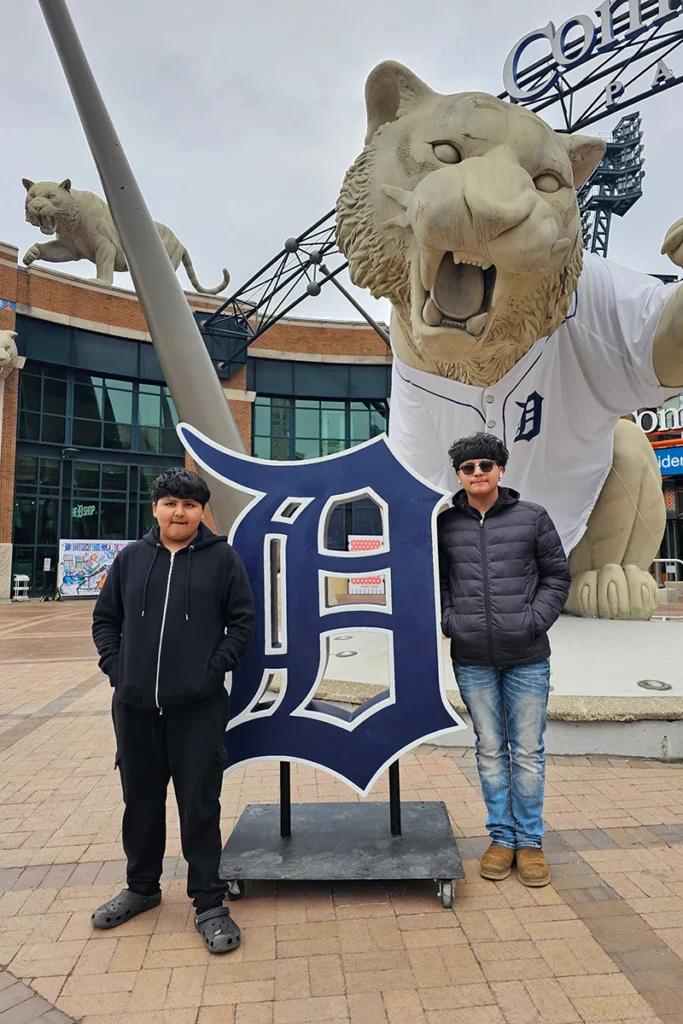 Two people posing by Detroit Tigers statue and logo at Comerica Park.