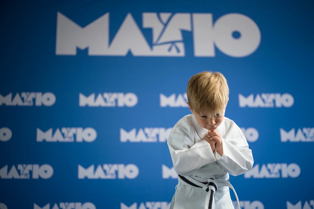 Young boy in martial arts uniform bowing with hands clasped.